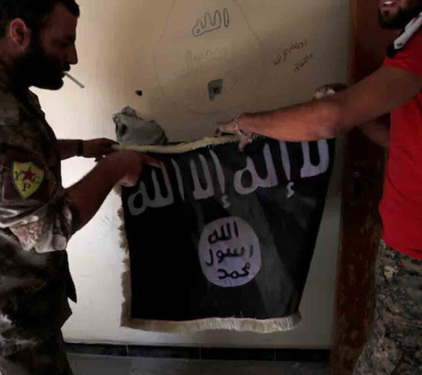 Members of Syrian Democratic Forces hold a flag of the Islamic State militants recovered at a building next to the stadium in Raqqa, Syria.