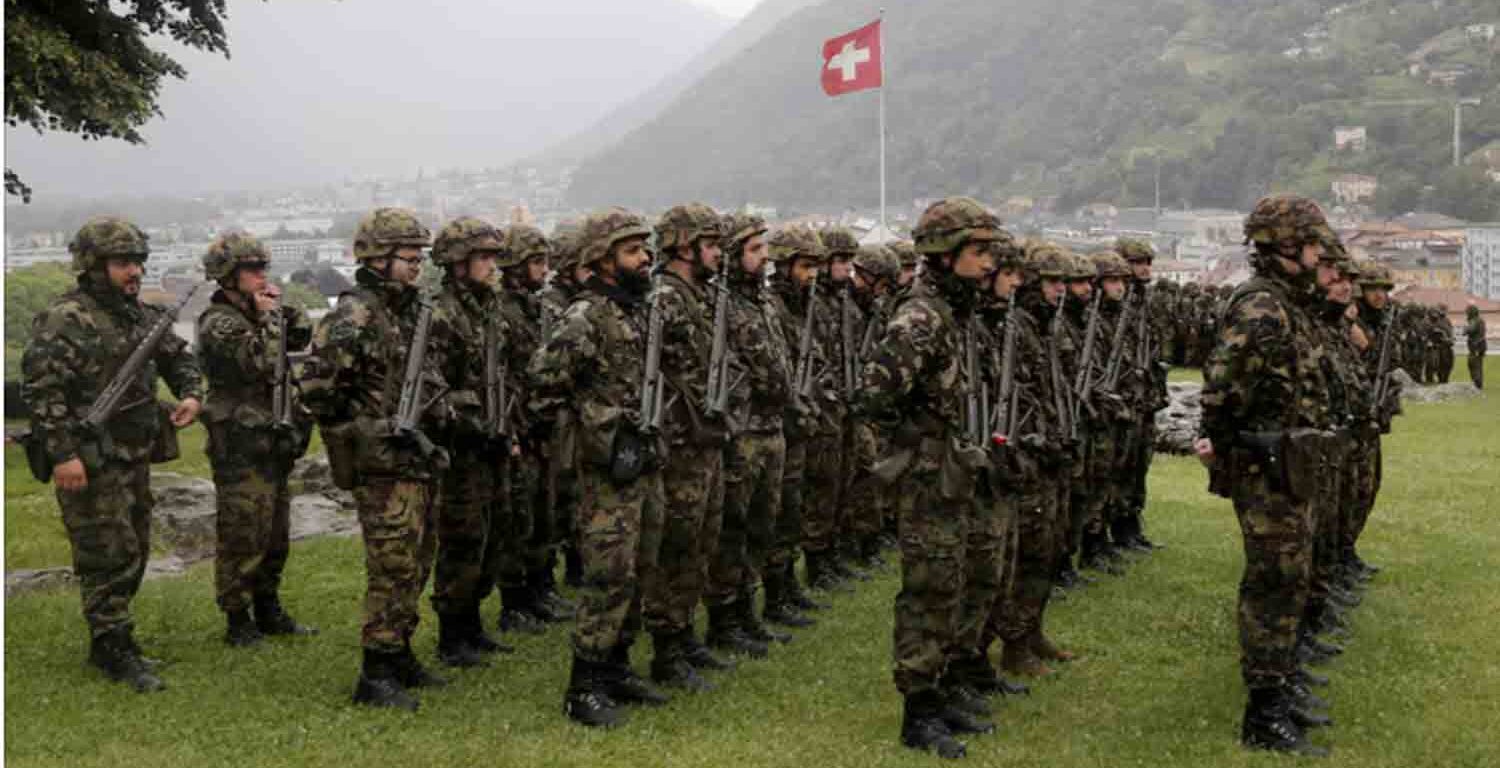 Switzerland's national flag flies behind soldiers of the Swiss Army's 21st Signal Battalion before a ceremony at the medieval Castelgrande castle in Bellinzona, Switzerland.