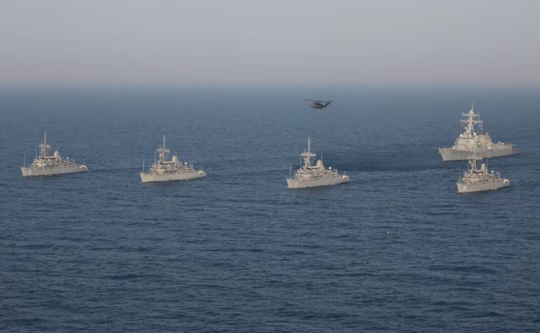 A formation of Avenger-class mine countermeasure ships USS Devastator (MCM 6), USS Gladiator (MCM 11), USS Sentry (MCM 3), USS Dextrous (MCM 13), the Arleigh Burke-class guided missile destroyer USS Mason (DDG 87) and an MH-53E Sea Dragon helicopter assigned to the “Blackhawks” of Helicopter Mine Countermeasures Squadron (HSM) 15 maneuver in the Arabian Sea.