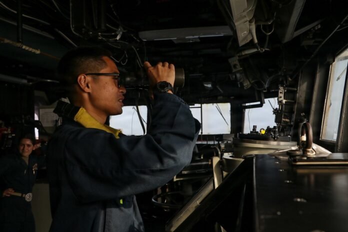 A U.S. sailor stands watch aboard USS Frank E. Petersen Jr. (DDG 121) as the ship patrols the Arabian Sea supporting the U.S. blockade against Iran. CENTCOM has redirected 17 commercial vessels, disabled 2, and boarded 2 to ensure compliance.